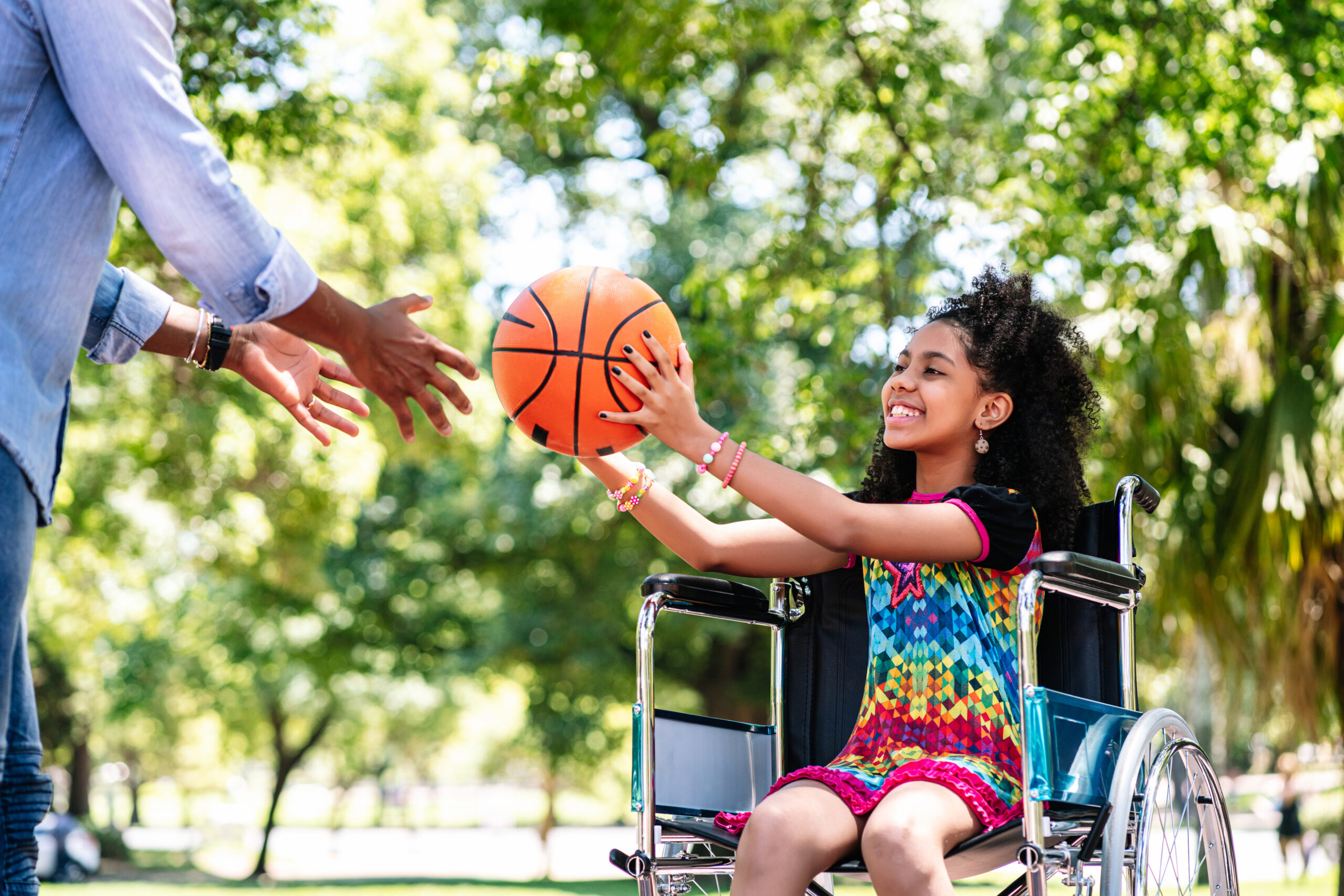 little girl in a wheelchair playing basketball with her father.
